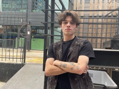 Matthew Sturniolo is wearing a black tee with sleeveless black jacket and posing with his hands crossed.